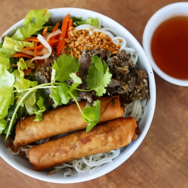 A bowl of Vietnamese vermicelli noodles with spring rolls, beef, and fresh vegetables.