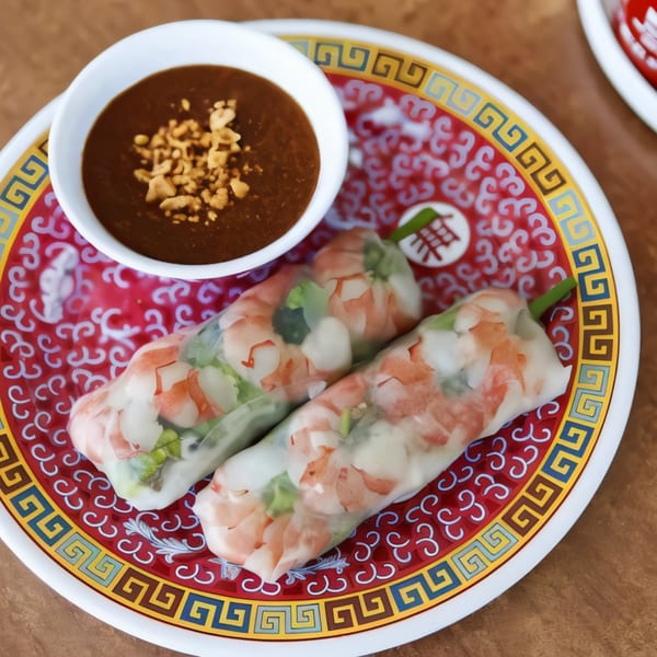 Two fresh spring rolls with shrimp and vegetables, served with peanut sauce on a decorative plate.