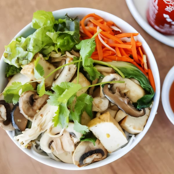 A white bowl filled with mushrooms, tofu, carrots, and greens, with a side of red sauce.